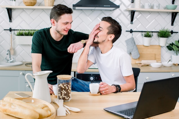 Casal gay feliz tomando café e se divertindo juntos. Rotina diária da vida do casal gay na cozinha de casa. Conceito gay, vida feliz