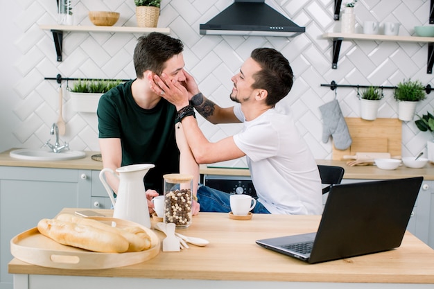 Casal gay feliz tomando café e se divertindo juntos. Rotina diária da vida do casal gay na cozinha de casa. Conceito gay, vida feliz