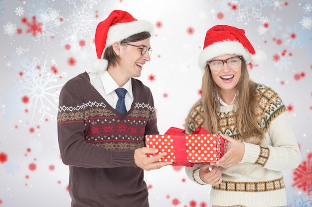 Foto casal geeky hipster segurando presente contra padrão de floco de neve