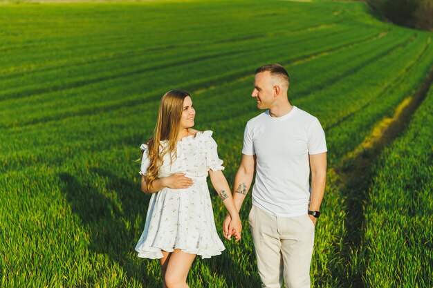 Casal grávida abraçando em um campo verde primavera Pais expectantes no parque de árvores floridas brancas Um casal romântico esperando um bebê Um passeio por um campo verde