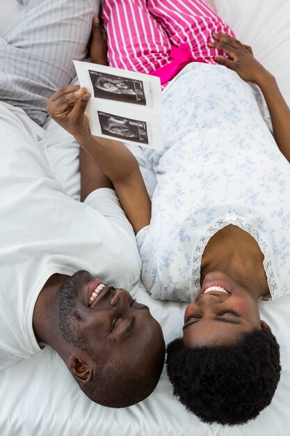 Casal grávida deitada na cama e olhando para a ultra-sonografia