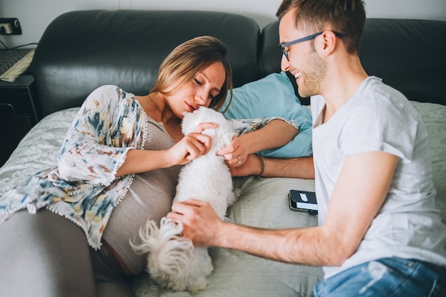 Casal grávida deitada na cama relaxante com cachorrinho