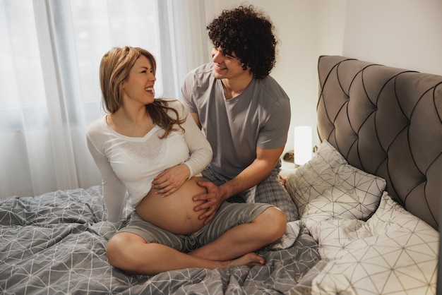 Casal grávida feliz apaixonado relaxando em uma cama no quarto.