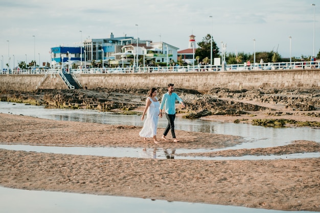 Casal grávida tirando fotos na praia ao pôr do sol