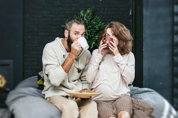 Casal heterossexual lindo jovem e uma mulher grávida tomando café da manhã na cama, no quarto de casa