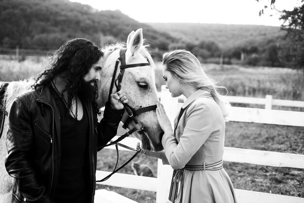 Casal homem e mulher andando em um rancho com cavalo puro-sangue Linda garota usando vestido rosa e cara vestido de cowboy As pessoas estão felizes e se divertindo