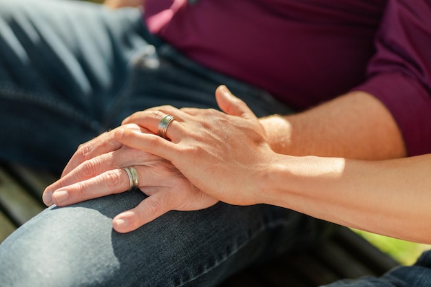 Foto casal homossexual sentado no banco de mãos dadas com foco seletivo em anéis closeup