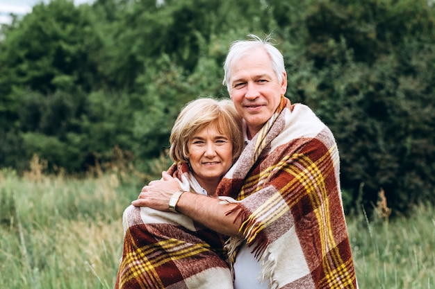 Casal idoso caminha na natureza e se abraça