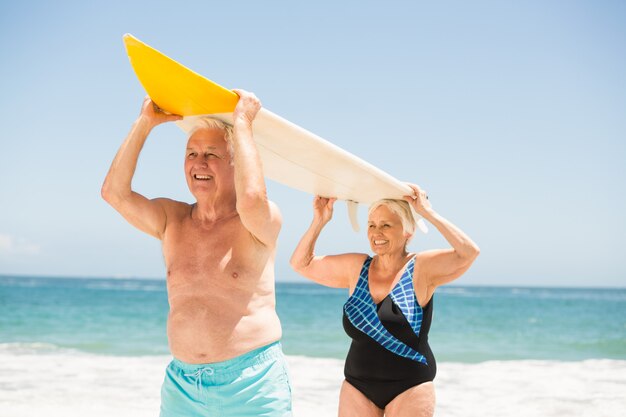 Casal Idoso carregando uma prancha de surf