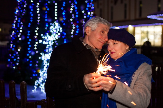 Casal idoso da família queimando fogos de artifício para iluminação do feriado à noite de natal e ano novo