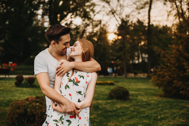 Casal incrível se abraçando e olhando sorrindo enquanto namorava contra o pôr do sol no parque.