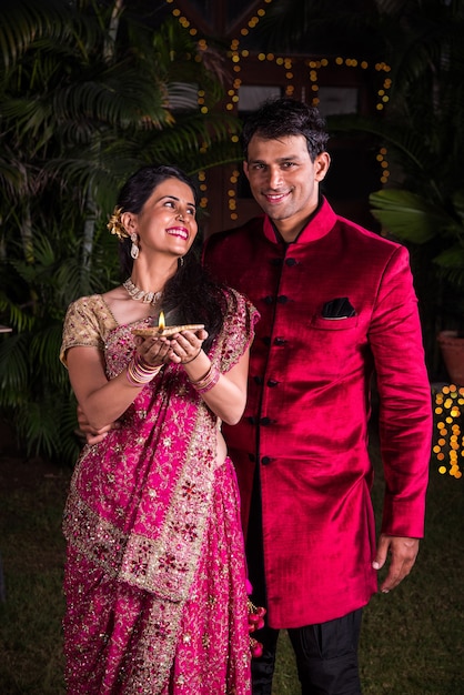 Casal indiano bonito com roupas tradicionais segurando um prato cheio de Motichoor ou bundi laddu diya e puja thali, respectivamente, na Noite de Diwali