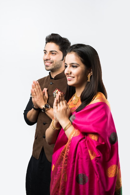 Casal indiano dando as boas-vindas com pose de namaskara ou ambas as mãos postas enquanto veste roupas tradicionais do festival, isolado sobre fundo branco