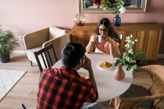 Casal indiano feliz tomando café da manhã e conversa fiada juntos na cozinha amizade namoro e família