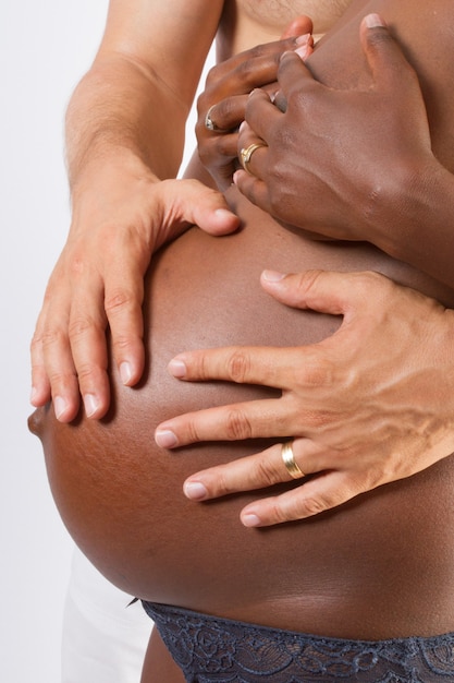 Casal inter-racial feliz, esposa afro-americana grávida e marido caucasiano acariciando a barriga do bebê