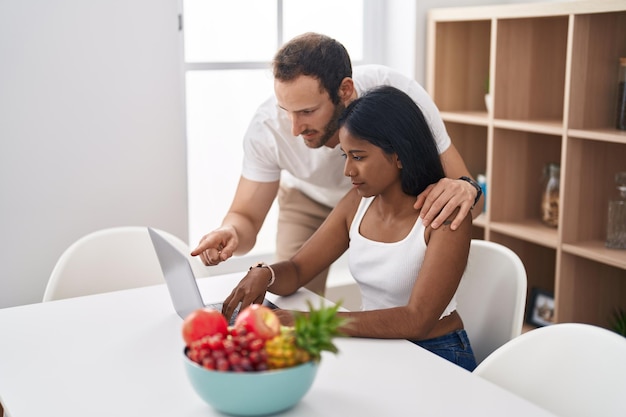 Casal interracial homem e mulher usando laptop sentado na mesa em casa