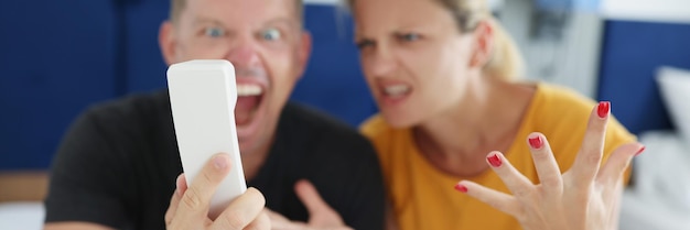 Casal irritado gritando ao telefone enquanto está sentado na cama no hotel closeup