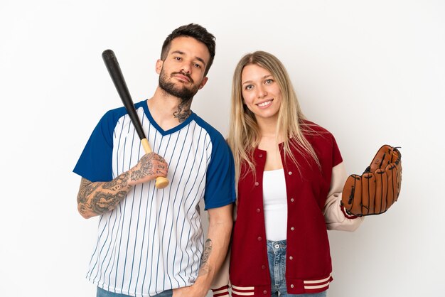 Casal jogando beisebol sobre fundo branco isolado, posando com os braços na cintura e sorrindo