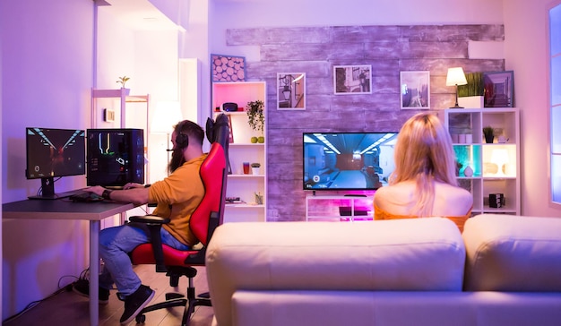 Casal jogando diferentes jogos de tiro em seu quarto com luz de néon colorida. Homem sentado na cadeira de jogos.