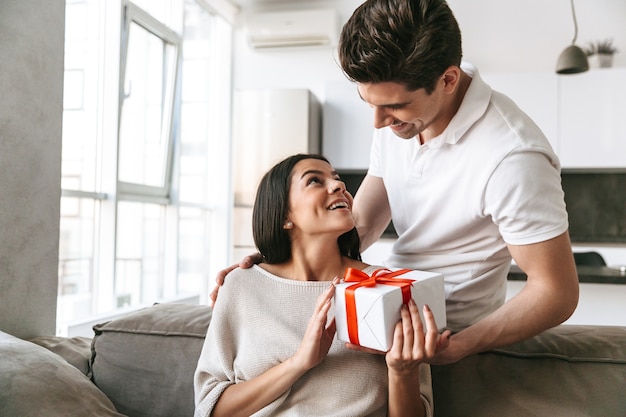 Casal jovem adorável e feliz comemorando juntos enquanto estão sentados em um sofá em casa