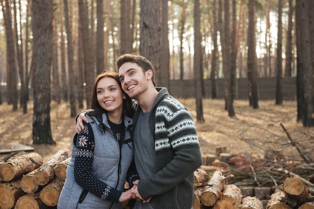 Casal jovem alegre, olhando para cima enquanto abraça e caminha na floresta