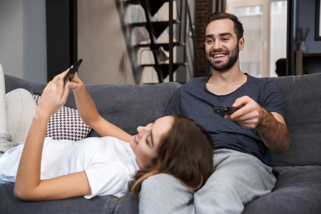 Casal jovem alegre relaxando no sofá em casa, assistindo tv