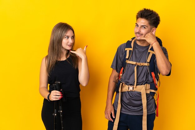Casal jovem alpinista com uma mochila grande em amarelo, fazendo gesto de telefone. ligue-me de volta sinal