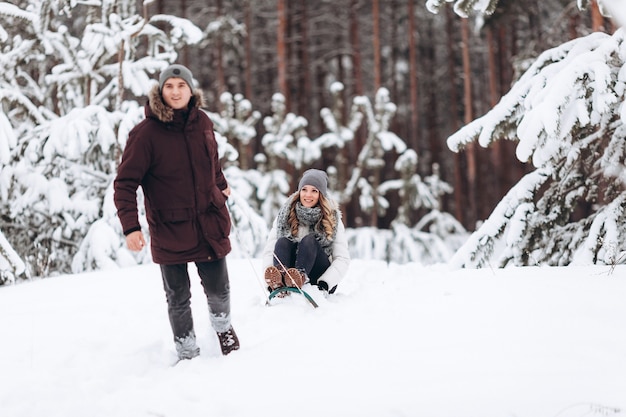 Casal jovem andando de trenó e curtindo o ar livre enquanto cai neve