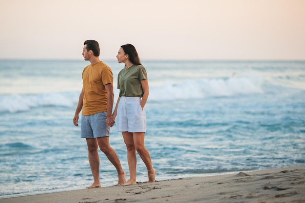 Casal jovem andando na praia férias de verão Feliz homem e mulher olham para o mar