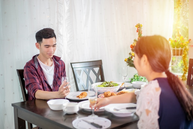 Casal jovem asiático, desfrutando de uma noite de jantar romântico bebe enquanto está sentado na mesa de jantar na cozinha juntos