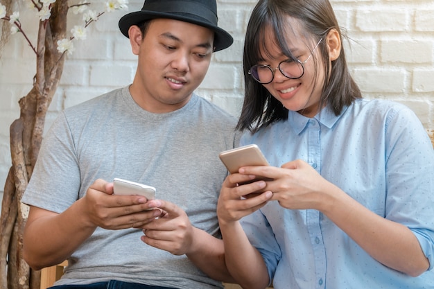 Casal jovem asiático falando e usando o telefone móvel esperto com ação de felicidade