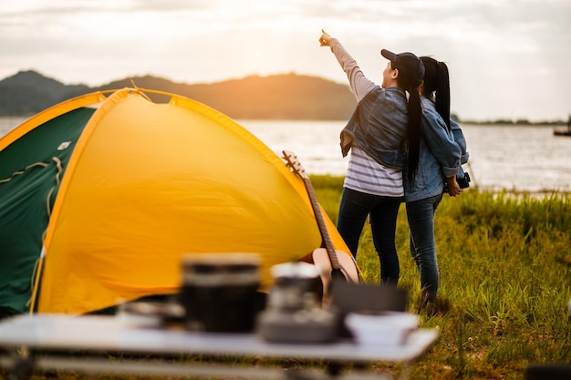 Casal jovem asiático feliz sentado na cadeira de piquenique bebendo chá e café enquanto acampamento à beira do lago