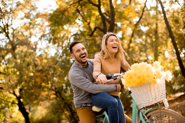 Casal jovem ativo desfrutando de andar de bicicleta no parque outono dourado