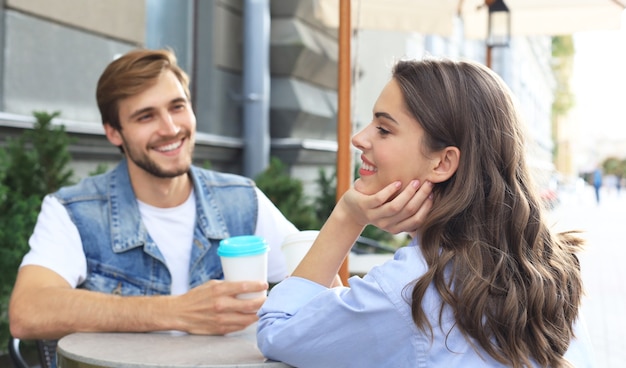 Foto casal jovem atraente apaixonado, bebendo café enquanto está sentado à mesa do café ao ar livre.