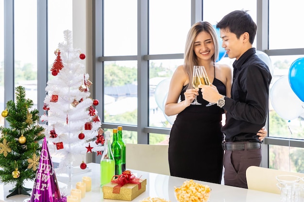 Casal jovem atraente celebra o Natal e o Ano Novo na festa tinindo taça de champanhe com lanche e bebida na mesa