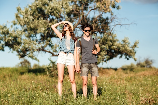 Casal jovem atraente hippie em pé contra árvores ao fundo e de mãos dadas