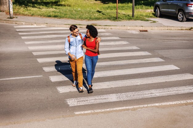 Casal jovem atraente multicultural hippie feliz abraçando e atravessando a rua.