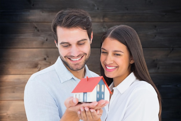 Casal jovem atraente segurando uma casa modelo contra o fundo de pranchas de madeira