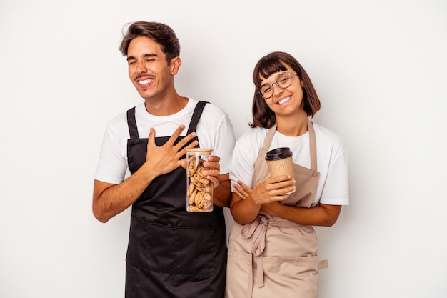 Casal jovem balconista de raça mista isolado no fundo branco, rindo e se divertindo.