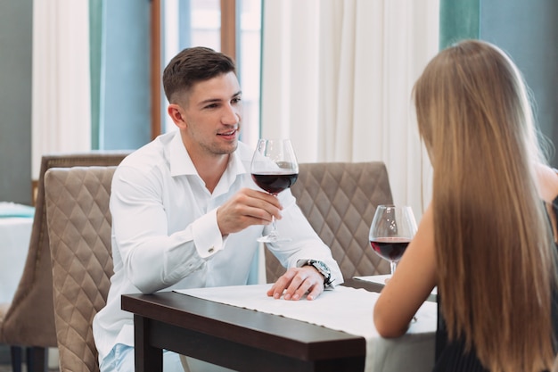 Casal jovem bonito com copos de vinho tinto no restaurante de luxo