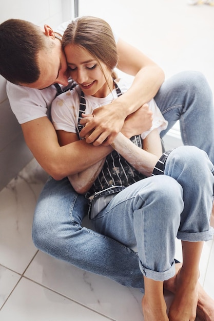 Casal jovem bonito em jeans sentado no chão e abraçando uns aos outros