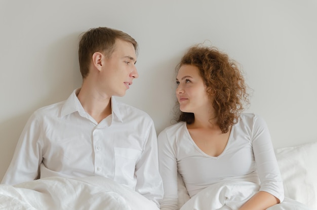 Casal jovem bonito sentado na cama juntos e olhando um ao outro