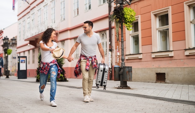 Casal jovem brincalhão é se divertir na rua enquanto carregando bolsa e um chapéu.