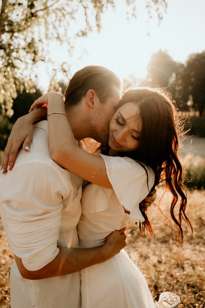 Casal jovem caminhando e beijando no prado de verão ao pôr do sol