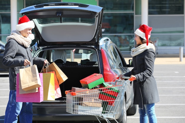 Casal jovem carregando compras de natal no porta-malas do carro no estacionamento do shopping