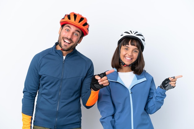 Casal jovem ciclista isolado no fundo branco, apontando o dedo para o lado e apresentando um produto