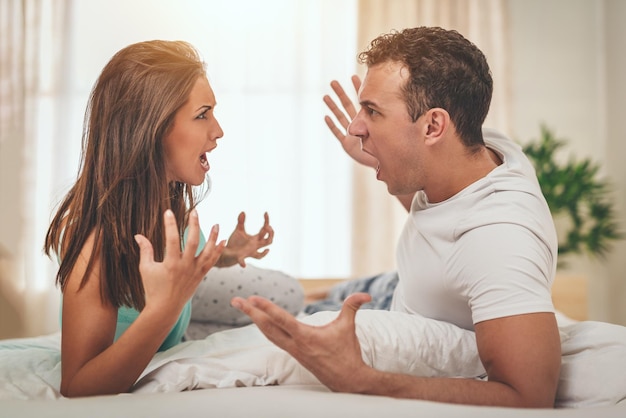 Casal jovem com raiva está tendo uma discussão na cama. Eles estão gritando um com o outro.