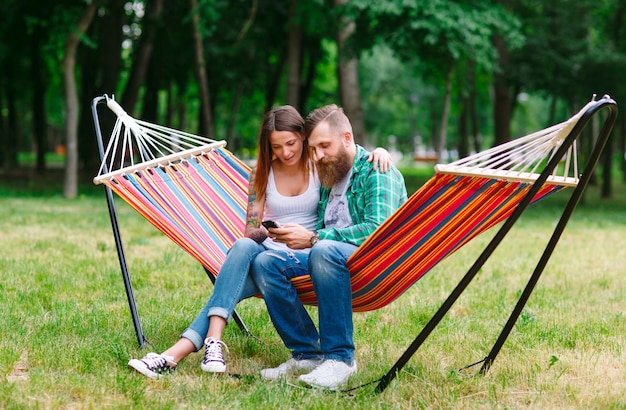 Casal jovem com telefone móvel, sentado na rede