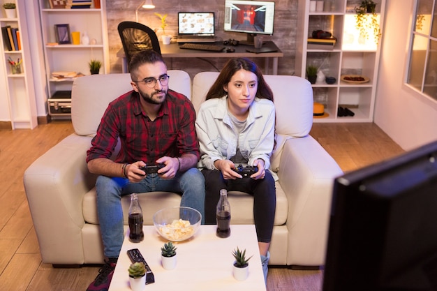 Casal jovem concentrado enquanto jogava videogame na televisão. Casal sentado no sofá.