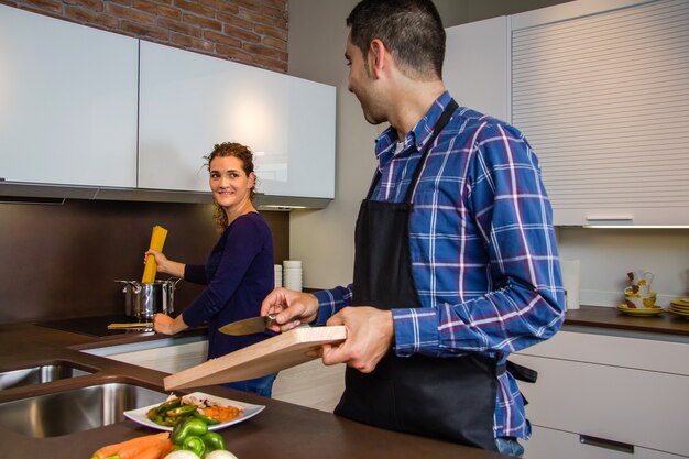 Casal jovem cortando vegetais na cozinha para preparar comida